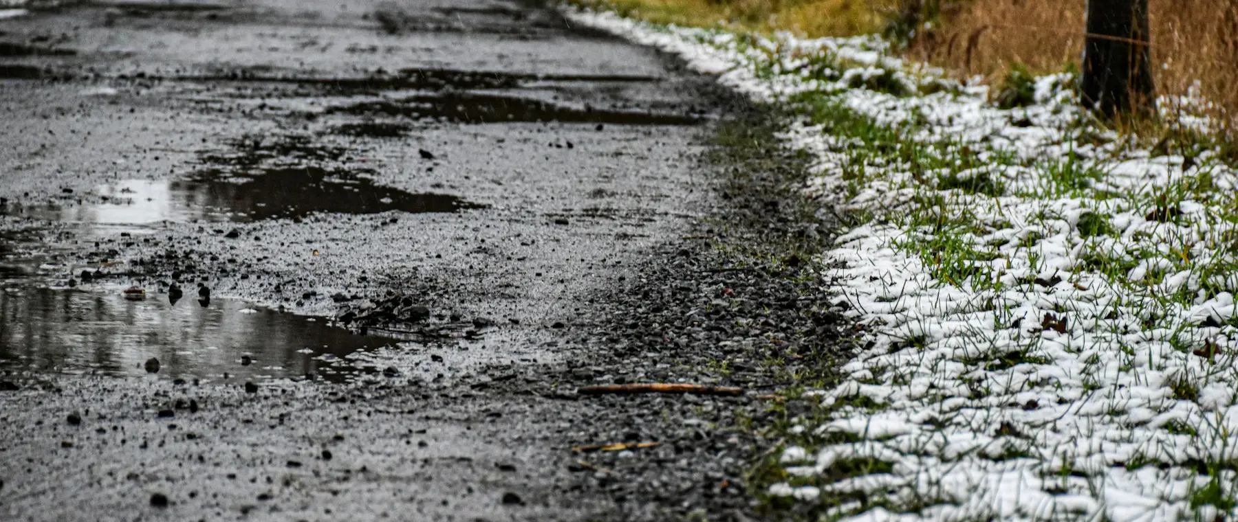 Wet lane with standing water and melting snow along the verge