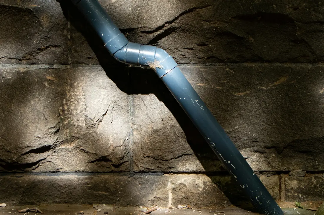 Downspout discharging straight onto the ground at the base of a stone wall