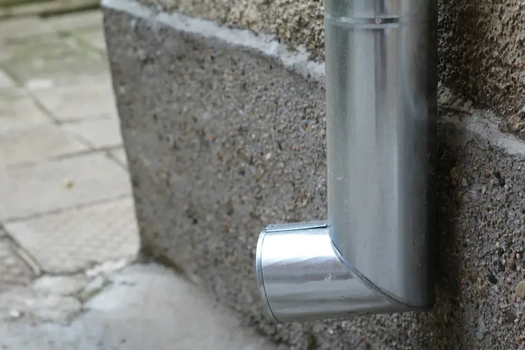 Downspout elbow discharging at the base of a wall onto a paved surface