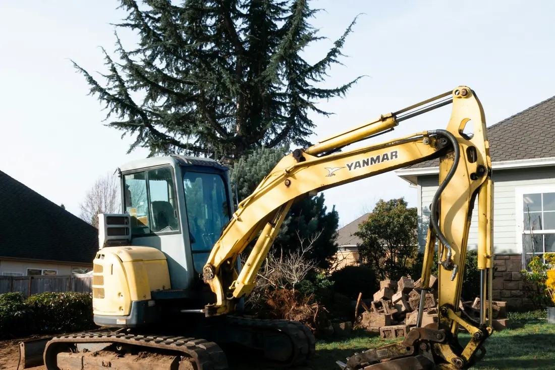 Compact excavator parked beside a house, the machine size most residential trenches need
