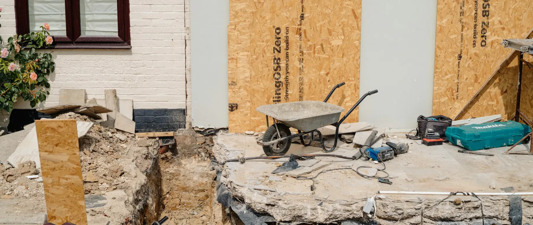 Foundation excavation beside a house with drainage materials laid out on the ground