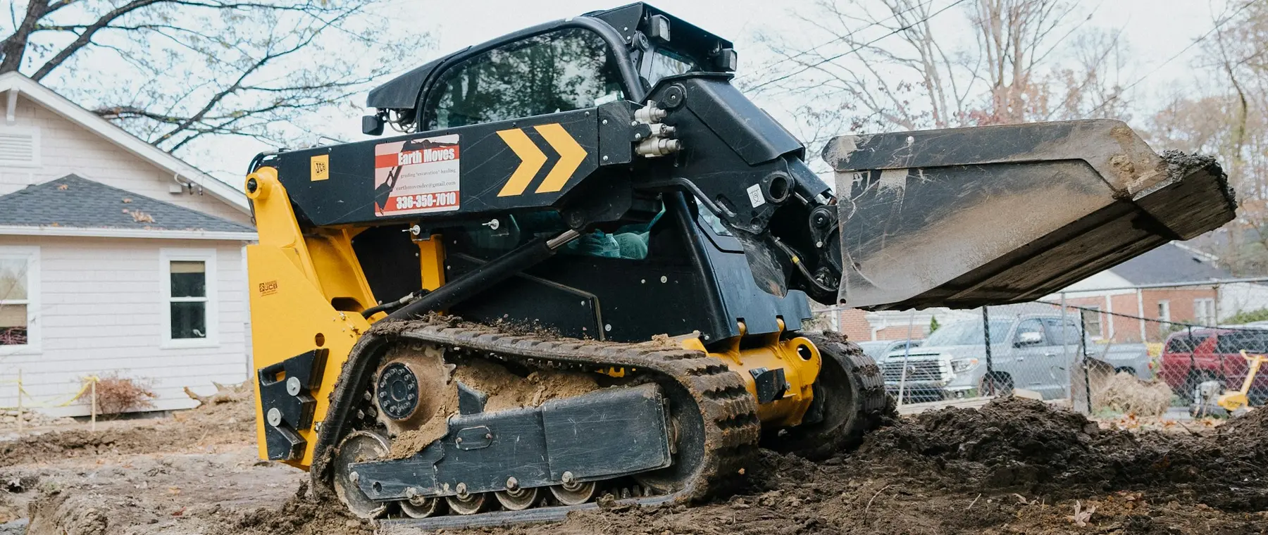 Compact track loader working beside a house on a residential lot