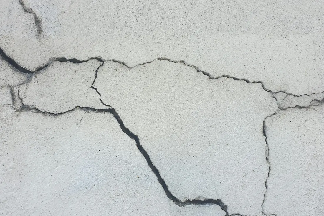 Fine branching cracks across a light-coloured concrete wall surface
