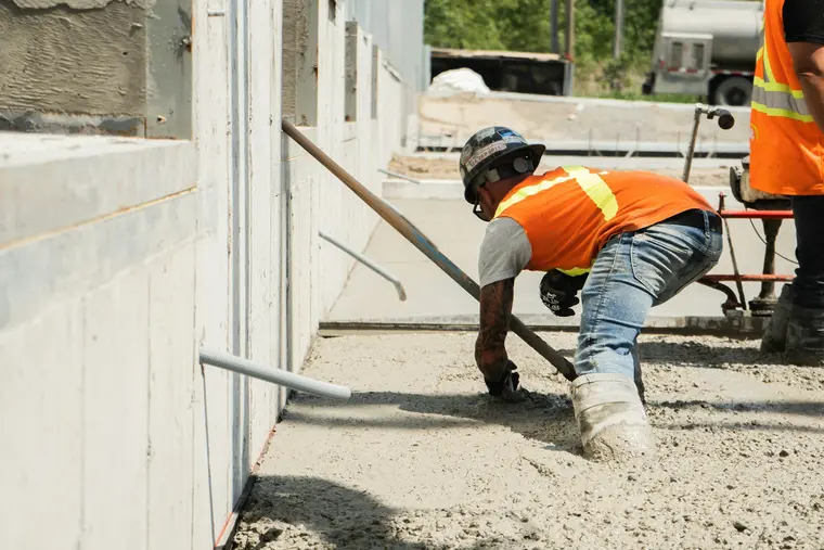 Worker screeding fresh concrete beside a house foundation wall