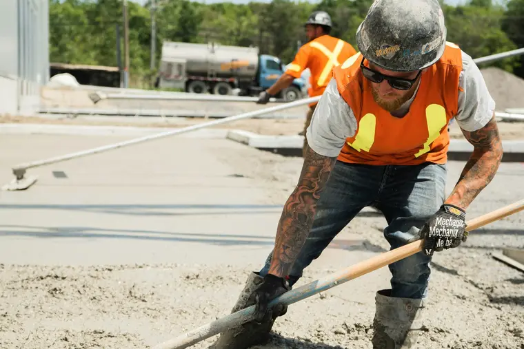 Worker screeding fresh concrete level with a straightedge